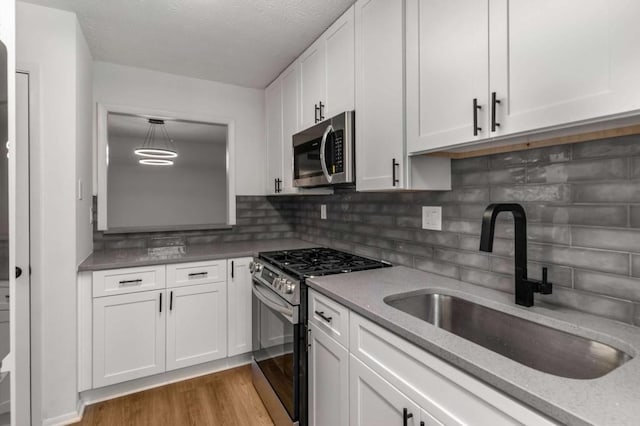 kitchen with wood finished floors, a sink, stainless steel appliances, white cabinetry, and backsplash