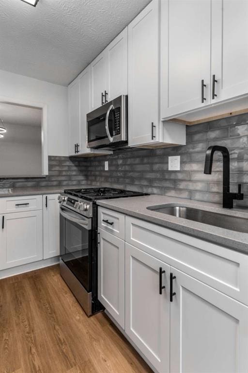 kitchen featuring light wood finished floors, a sink, decorative backsplash, stainless steel appliances, and white cabinetry