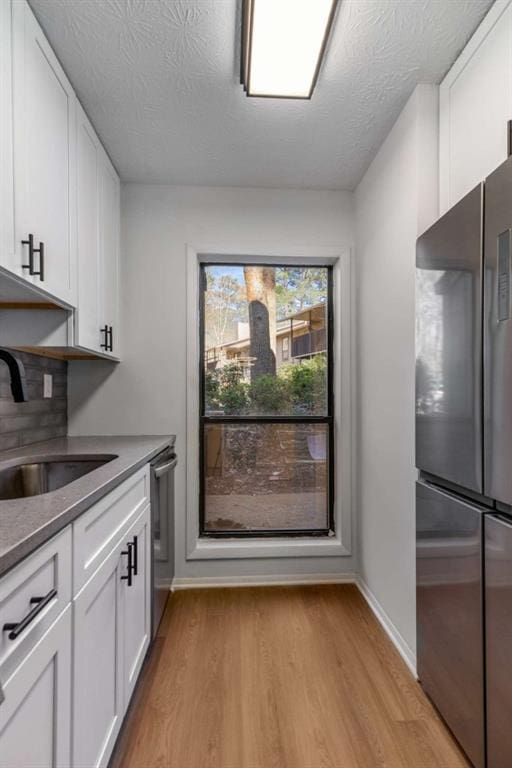 kitchen with light wood-style flooring, a sink, a textured ceiling, white cabinetry, and appliances with stainless steel finishes