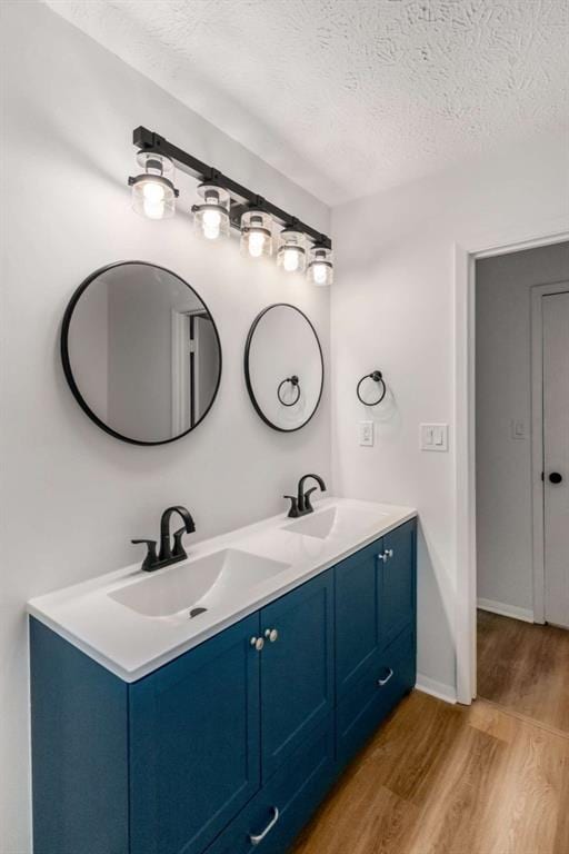 bathroom featuring a sink, a textured ceiling, wood finished floors, and double vanity