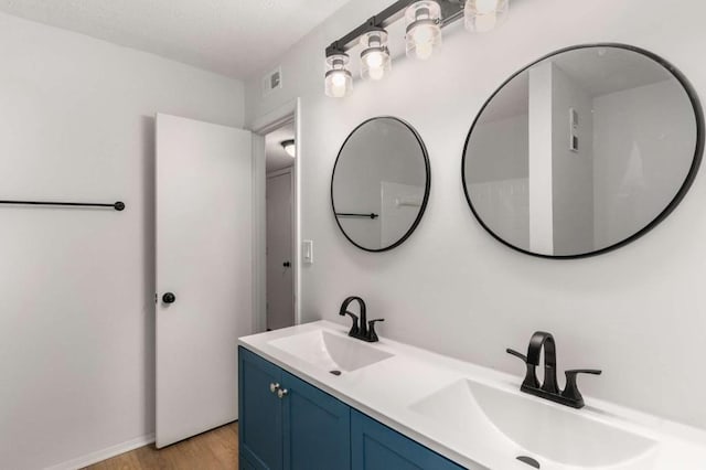 bathroom with a sink, visible vents, wood finished floors, and double vanity