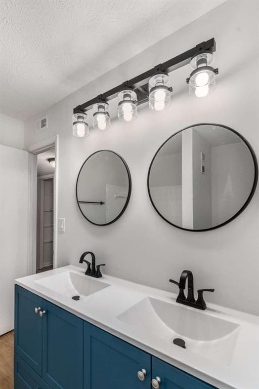 full bath with double vanity, wood finished floors, a textured ceiling, and a sink