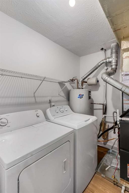 laundry room featuring water heater, laundry area, light wood-style flooring, independent washer and dryer, and a textured ceiling