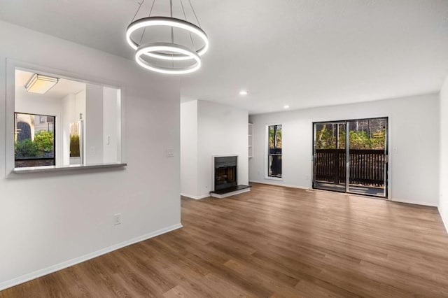 unfurnished living room with recessed lighting, a fireplace with raised hearth, baseboards, and wood finished floors