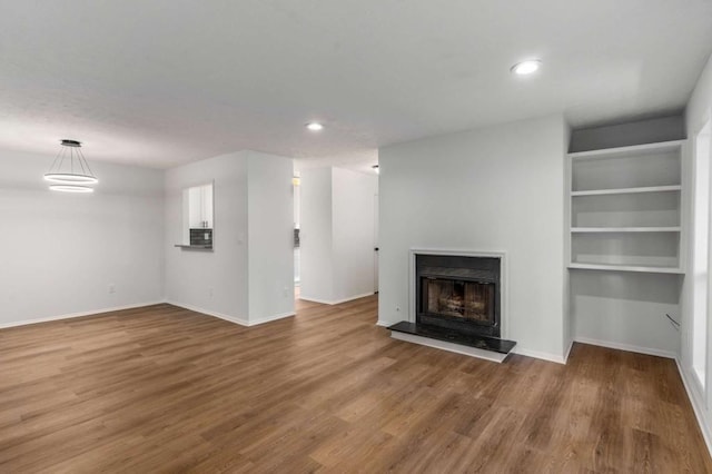 unfurnished living room featuring a fireplace with raised hearth, baseboards, and wood finished floors