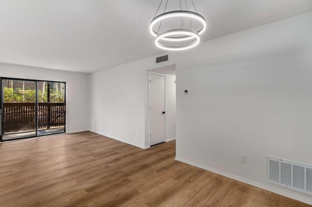 empty room with baseboards, wood finished floors, visible vents, and a chandelier