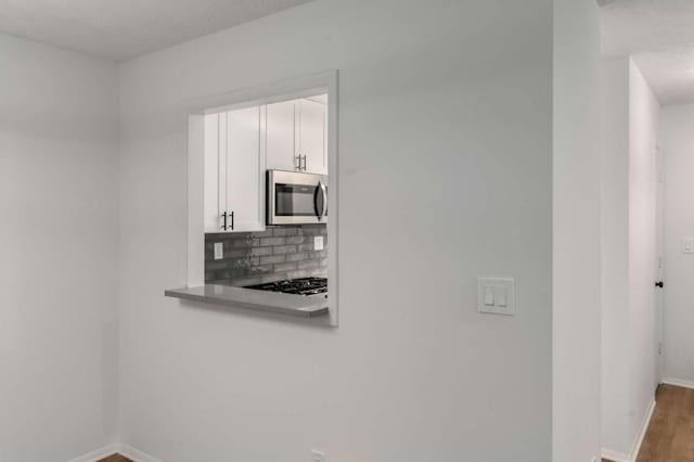 kitchen with wood finished floors, baseboards, decorative backsplash, white cabinets, and stainless steel microwave