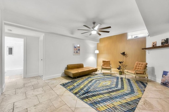 sitting room featuring ceiling fan, wooden walls, and baseboards