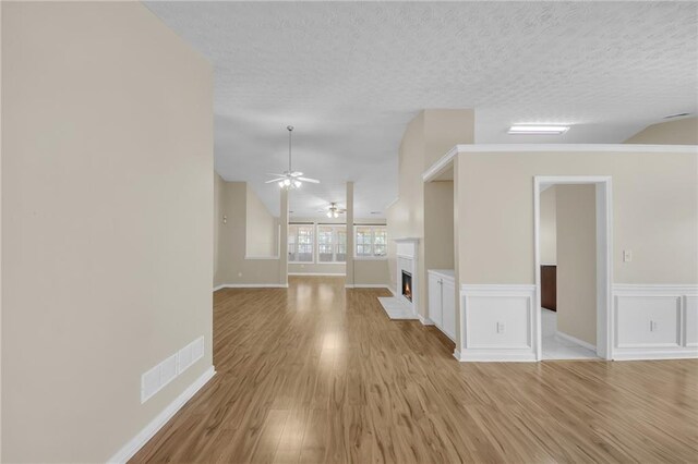 70 Prince Edward Way, Covington, GA 30016 - empty room with light wood-style flooring, ceiling fan, a warm lit fireplace, a textured ceiling, and wainscoting