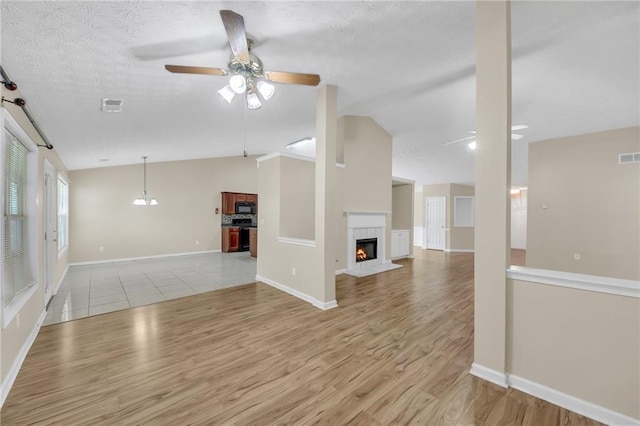 70 Prince Edward Way, Covington, GA 30016 - unfurnished living room with a ceiling fan, vaulted ceiling, light wood-style flooring, a warm lit fireplace, and a textured ceiling