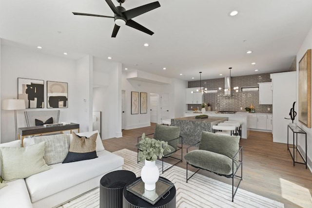 living room featuring recessed lighting, light wood finished floors, and ceiling fan with notable chandelier