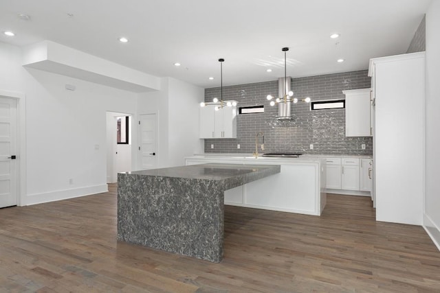 kitchen with a chandelier, white cabinetry, decorative backsplash, dark wood-type flooring, and a center island with sink