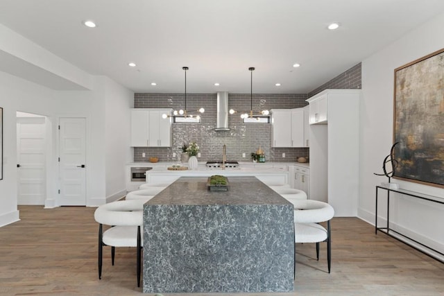 kitchen featuring wall chimney exhaust hood, white cabinetry, a breakfast bar area, and a kitchen island