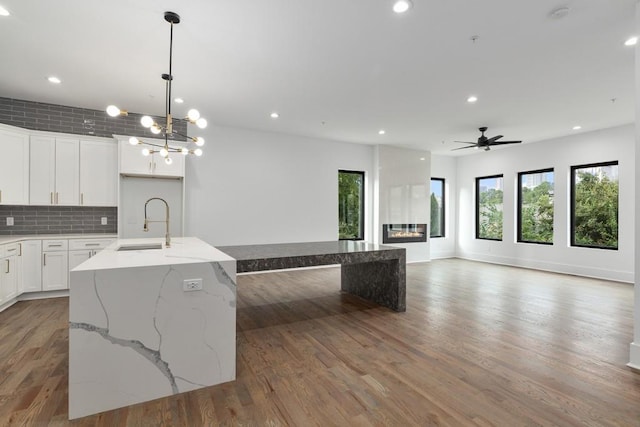 kitchen featuring open floor plan, a sink, light wood-style flooring, ceiling fan with notable chandelier, and backsplash