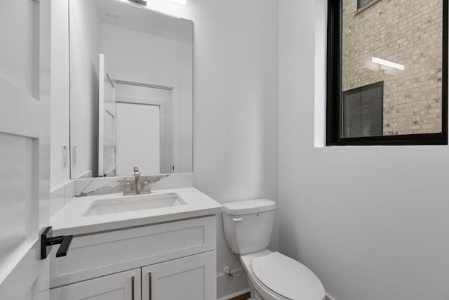 half bath featuring vanity, baseboards, and toilet