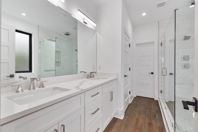bathroom featuring double vanity, visible vents, a stall shower, wood finished floors, and a sink