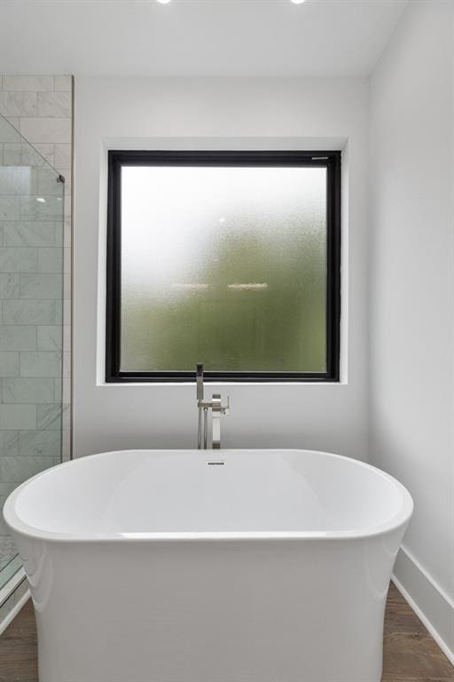 full bathroom featuring baseboards, a freestanding tub, wood finished floors, and a tile shower