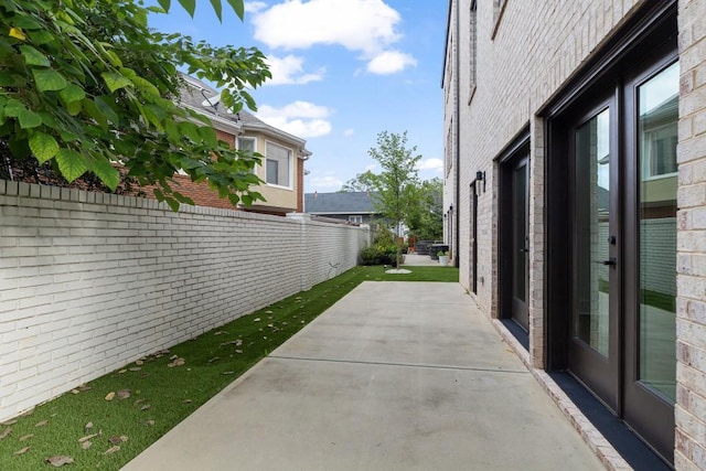 view of property exterior featuring brick siding, fence, and a patio area