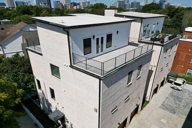 rear view of house with french doors, central AC unit, brick siding, a view of city, and a balcony