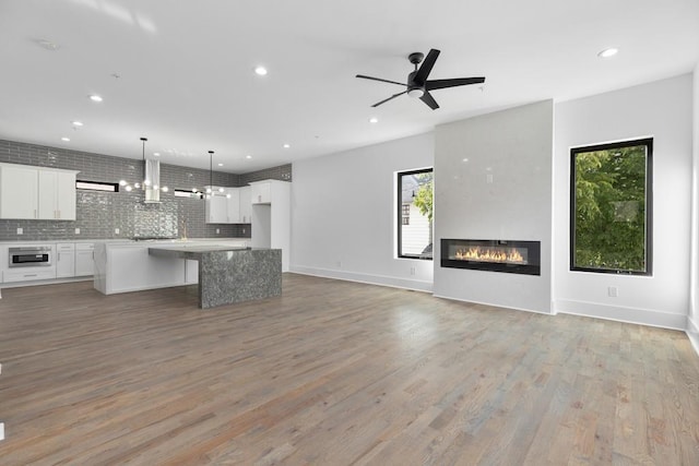 unfurnished living room featuring a glass covered fireplace, ceiling fan, recessed lighting, and light wood-style flooring