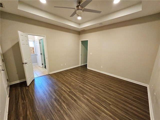 empty room featuring recessed lighting, a tray ceiling, baseboards, and wood finished floors