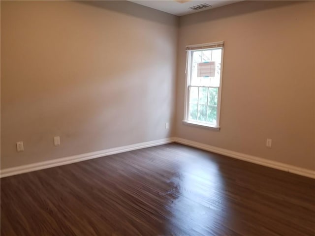 empty room with dark wood-style floors, baseboards, and visible vents