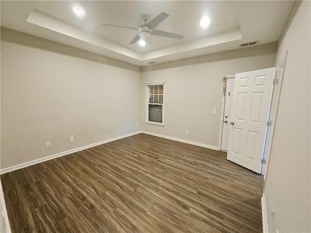 empty room with visible vents, a raised ceiling, dark wood-type flooring, and baseboards