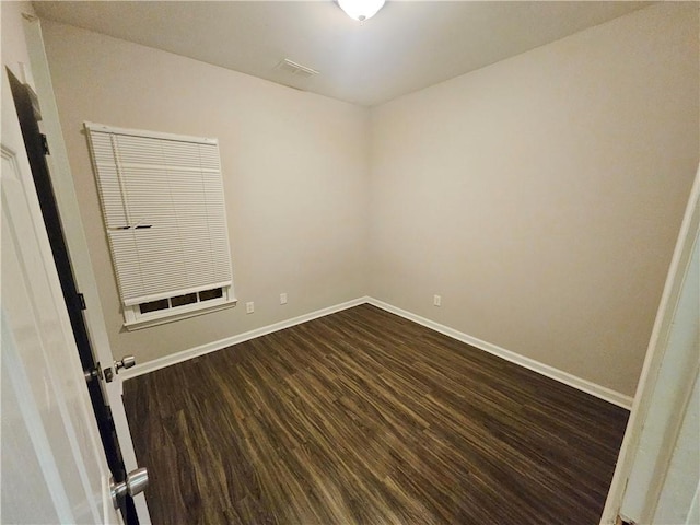 empty room with dark wood-style floors, visible vents, and baseboards