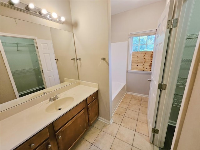 bathroom with a spacious closet, baseboards, a bath, tile patterned floors, and vanity