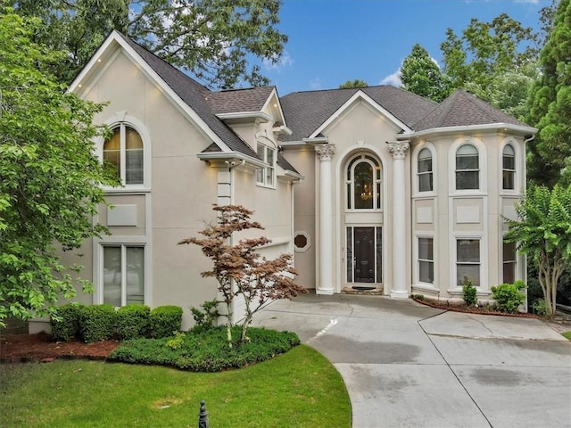 view of front of property featuring concrete driveway, a shingled roof, a front lawn, and stucco siding