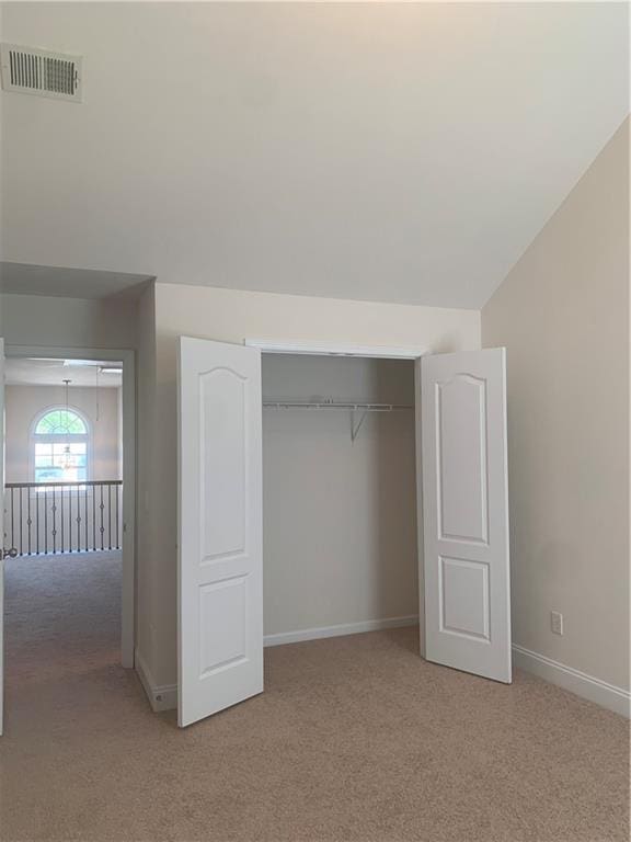 unfurnished bedroom featuring light colored carpet, vaulted ceiling, and a closet