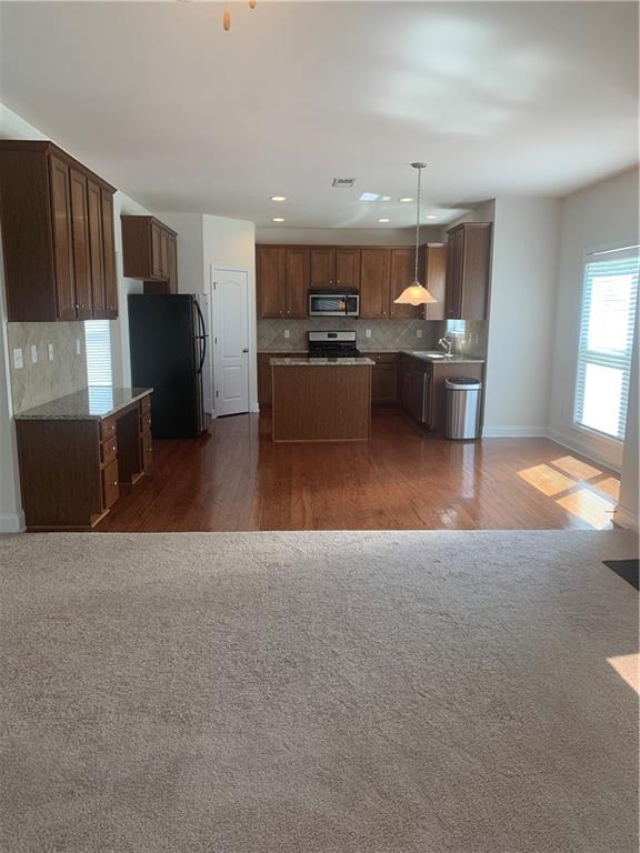 kitchen featuring decorative light fixtures, a kitchen island, black fridge, and dark wood-type flooring