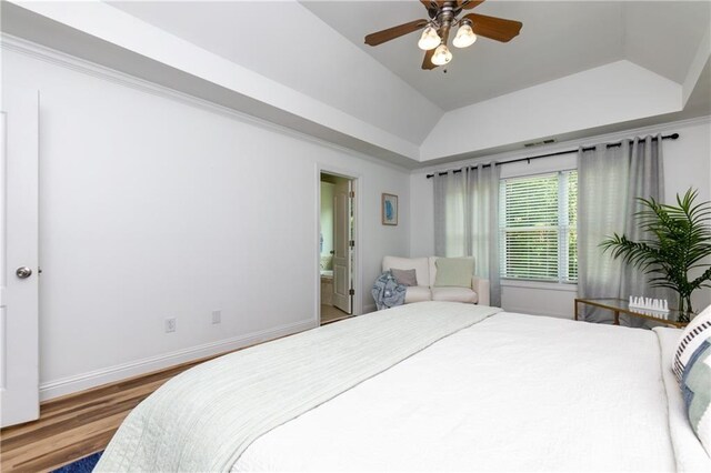 bedroom with lofted ceiling, a raised ceiling, ensuite bath, ceiling fan, and wood-type flooring