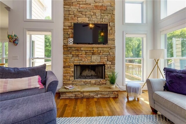 living room with wood-type flooring, a stone fireplace, and a high ceiling