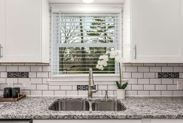 kitchen featuring backsplash, a sink, white cabinetry, and light stone countertops