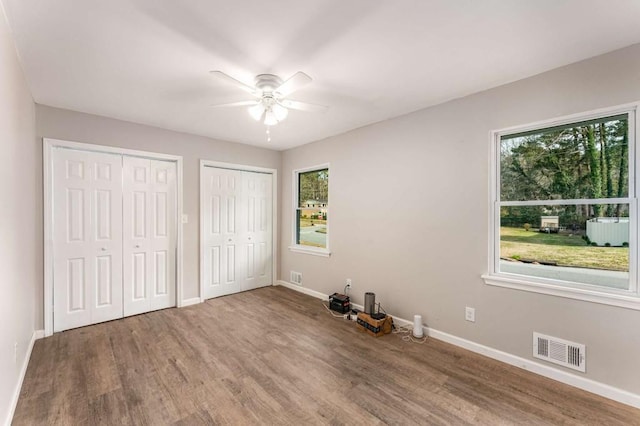 unfurnished bedroom with baseboards, wood finished floors, visible vents, and multiple closets