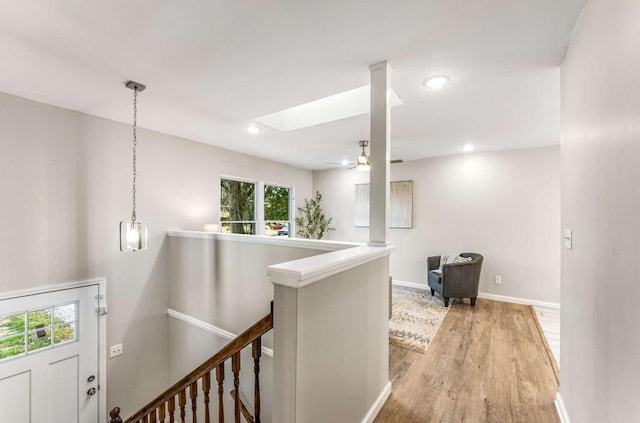 hall featuring a skylight, recessed lighting, light wood-style floors, an upstairs landing, and baseboards