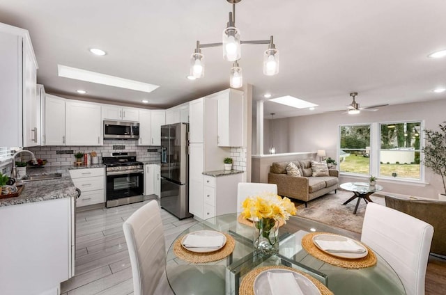 kitchen featuring a skylight, a sink, open floor plan, appliances with stainless steel finishes, and decorative backsplash