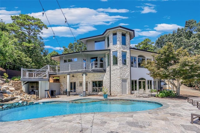 back of house with stone siding, a balcony, a pool with connected hot tub, and a patio