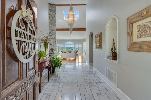 corridor featuring arched walkways, baseboards, visible vents, an inviting chandelier, and a high ceiling