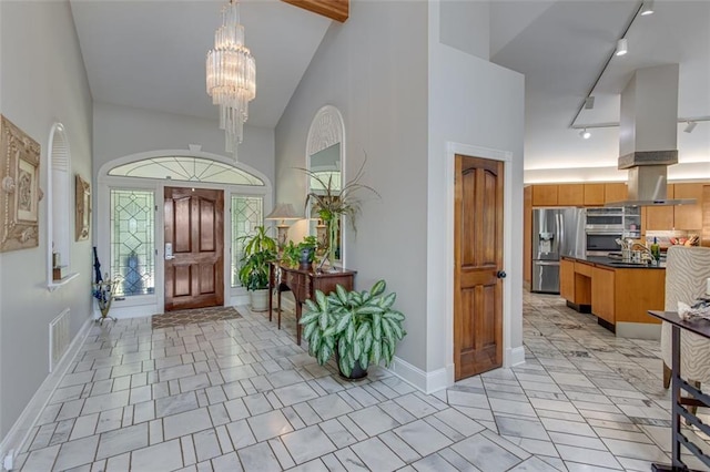 foyer featuring high vaulted ceiling, beam ceiling, light tile patterned floors, rail lighting, and an inviting chandelier