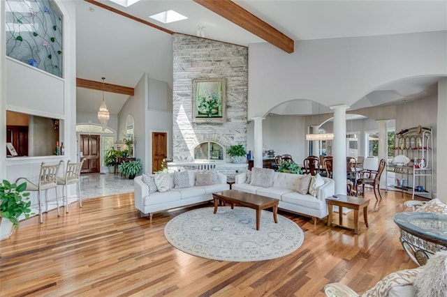 living room with wood finished floors, beam ceiling, a skylight, decorative columns, and high vaulted ceiling