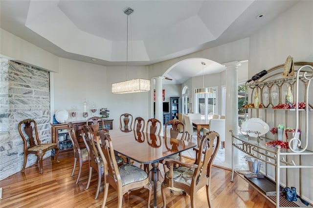 dining room with hardwood / wood-style floors, a raised ceiling, and decorative columns