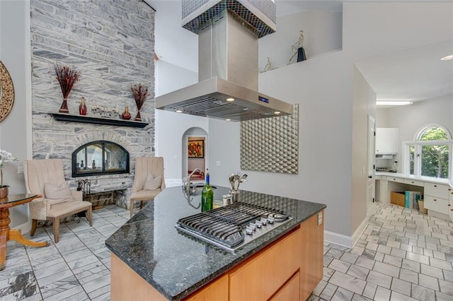 kitchen featuring stainless steel gas stovetop, island exhaust hood, a towering ceiling, dark stone countertops, and a kitchen island