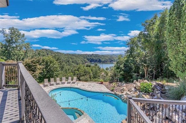 view of swimming pool featuring a patio area, a fenced in pool, a forest view, and a jacuzzi