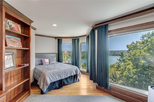 bedroom with light wood-type flooring, crown molding, and a water view