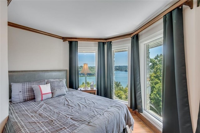 bedroom with hardwood / wood-style flooring, crown molding, a water view, and multiple windows