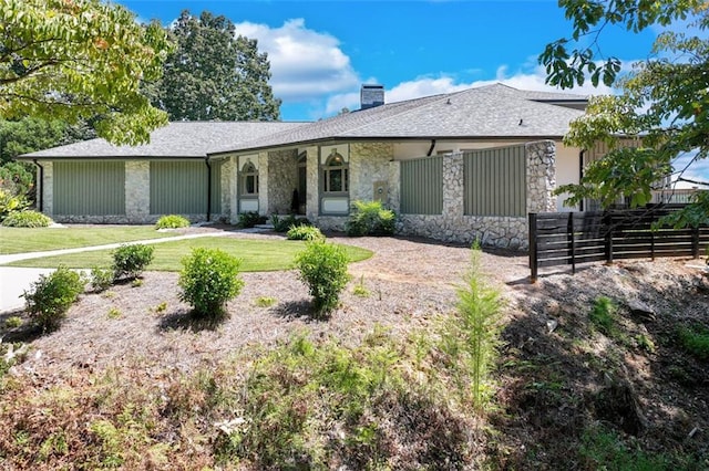 ranch-style home with a front lawn, stone siding, a chimney, and fence