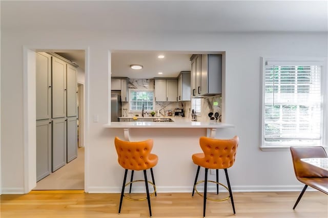 kitchen featuring a kitchen bar, stainless steel fridge, light wood-type flooring, and gray cabinets