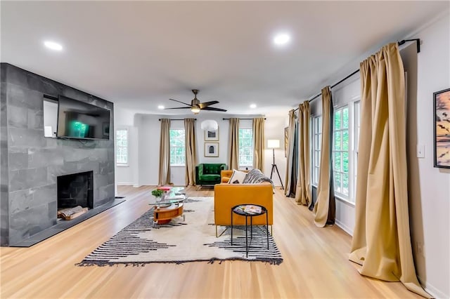 living room with a tile fireplace, light wood-type flooring, and ceiling fan